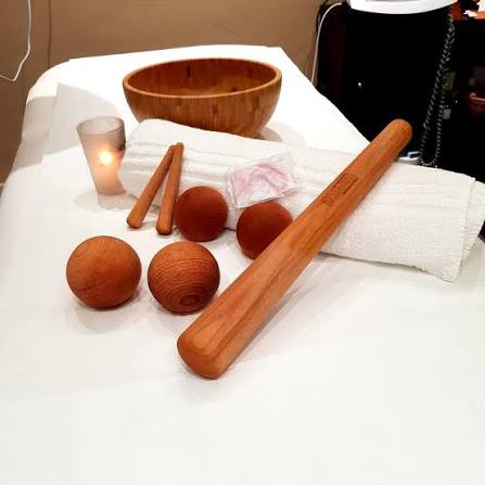 Strumenti per il massaggio Māori: sfere di legno, bastoncini, una ciotola e uno strumento lungo disposti sul lino.